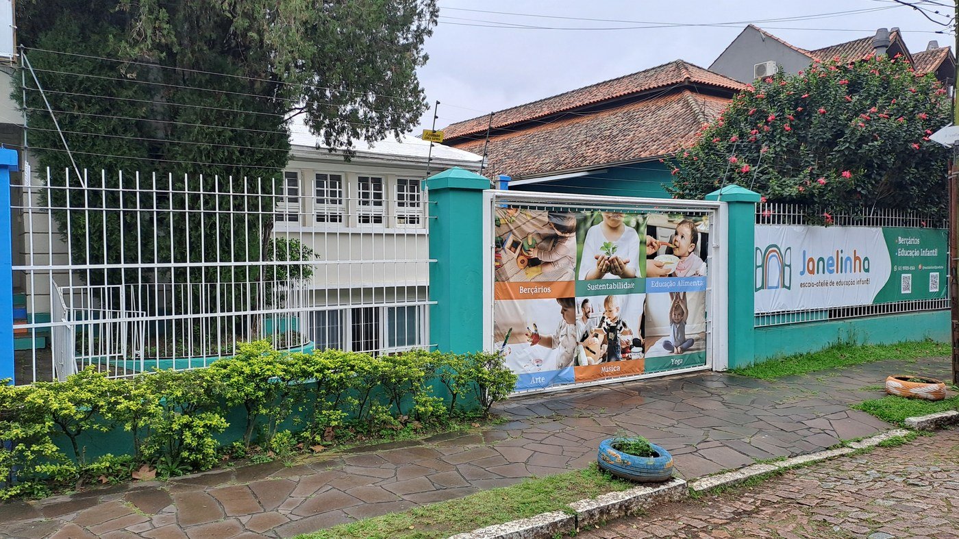 Fachada da Escola Janelinha em dia chuvoso, com o banner de atividades no portão